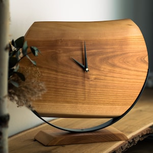 Peut inclure: Une horloge en bois avec des aiguilles noires et un support en métal noir. L'horloge est en bois brun clair avec un motif de grain naturel.