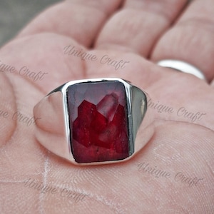 Op de afbeelding: Een zilveren ring met een grote, rechthoekige, rode edelsteen.