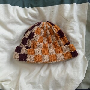 May include: A crocheted beanie hat with a checkered pattern in brown, beige, and orange.