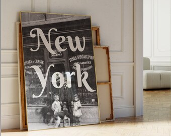 May include: A framed black and white print with the word "New York" in large, elegant script. The image depicts a vintage storefront with people and dogs. The print leans against a wall in a room with hardwood floors.