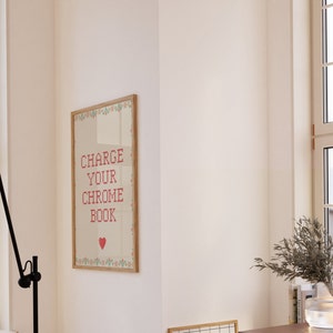 May include: A framed poster with the text "CHARGE YOUR CHROME BOOK" in red cross-stitch style lettering. The poster has a wooden frame and a decorative border with floral elements. A red heart is at the bottom.