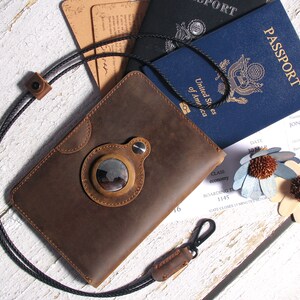May include: A brown leather passport holder with a circular window and a black strap. The holder is lying on a white wooden surface with a passport, boarding pass, and two decorative flowers.