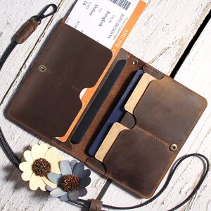 May include: A brown leather travel wallet with a black strap and multiple card slots. The wallet is open and contains a passport, boarding pass, and credit cards.