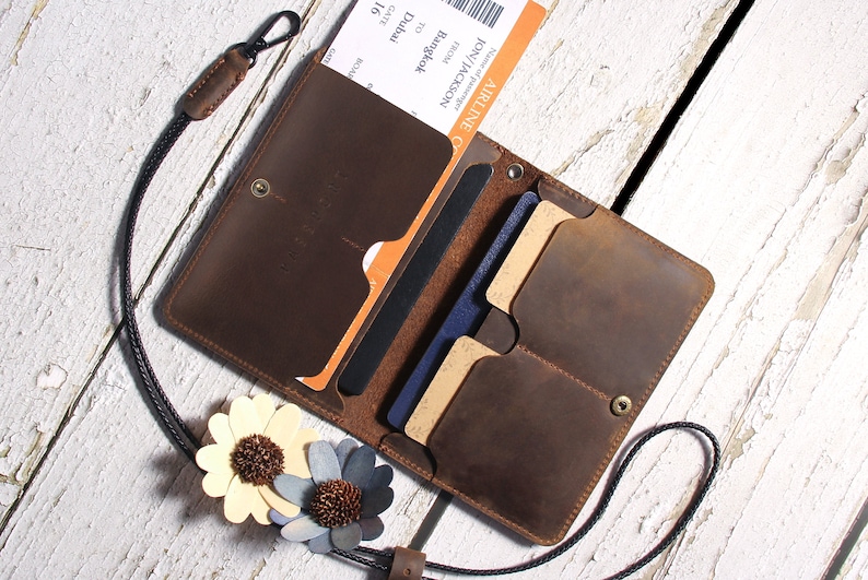 May include: A brown leather travel wallet with a black strap and multiple card slots. The wallet is open and contains a passport, boarding pass, and credit cards.