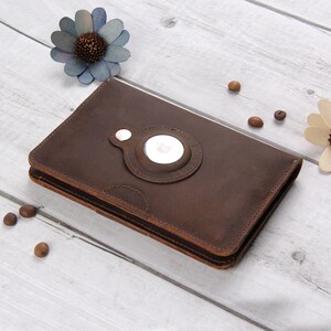 May include: A brown leather case with a circular cutout for a phone or tablet. The case has a magnetic closure and a stitched design.