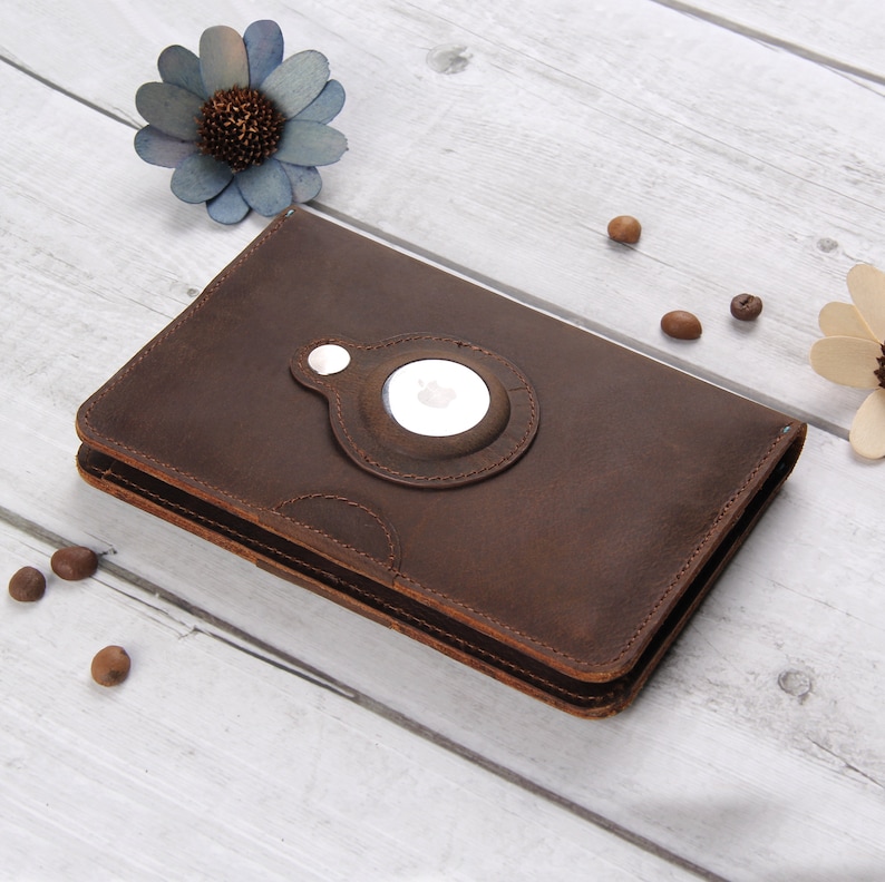 May include: A brown leather case with a circular cutout for a phone or tablet. The case has a magnetic closure and a stitched design.