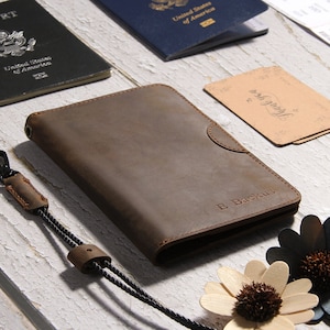 May include: A brown leather passport holder with a black strap and a silver clasp. The holder has the name "E. Backus" embossed on the front.