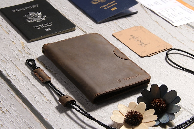 May include: A brown leather passport holder with a black strap and a silver clasp. The holder has the name "E. Backus" embossed on the front.