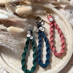 Könnte beinhalten: Drei Makramee-Schlüsselanhänger in Grün, Türkis und Koralle. Jeder Schlüsselanhänger hat ein Spiraldesign und einen Metallverschluss. Kleine, runde Anhänger mit Buchstaben hängen daran.