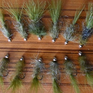 Puede incluir: Una colección de 12 señuelos de pesca con mosca verdes y plateados con colas de plumas.