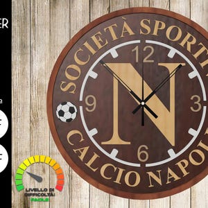 Puede incluir: Un reloj de madera marrón con una esfera blanca y detalles dorados. El reloj presenta el texto "Società Sportiva Calcio Napoli" y una gran letra "N" en el centro. El reloj tiene una aguja de hora y minutos negra y dos balones de fútbol a cada lado de la esfera.