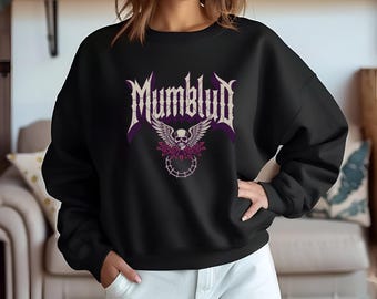 May include: Black sweatshirt featuring the word "Mumblud" in a gothic font above a skull with wings and floral accents. The design is in shades of purple and white. The sweatshirt is a crew neck style.