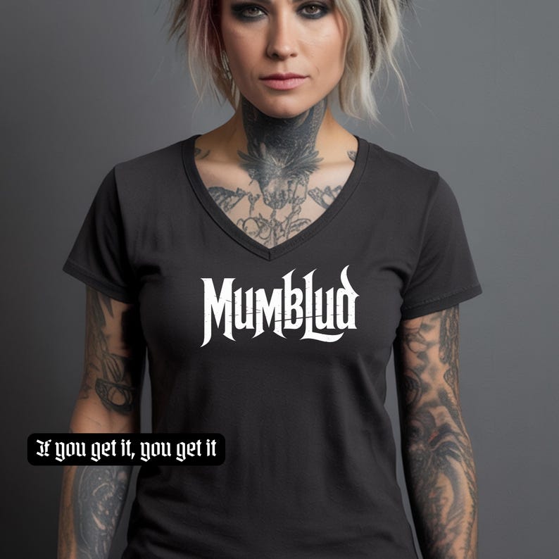 Puede incluir: Camiseta gris oscuro con cuello en V y texto blanco "MumbL&uuml;d" en fuente estilizada. Debajo, la frase "If you get it, you get it" en fuente g&oacute;tica m&aacute;s peque&ntilde;a. La camiseta tiene mangas cortas.