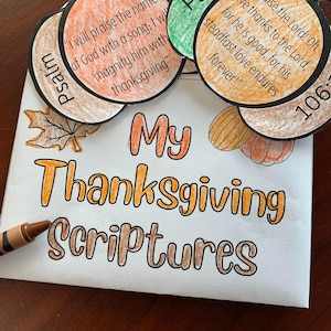 May include: A Thanksgiving-themed craft project featuring pumpkin-shaped cutouts with Bible verses and the title "My Thanksgiving Scriptures." The pumpkins are in shades of orange, brown, and green, with black outlines. A brown crayon is visible.