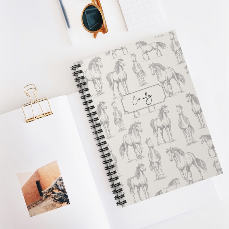 May include: A white spiral notebook with a grey horse pattern and the name "Emily" printed on the cover.