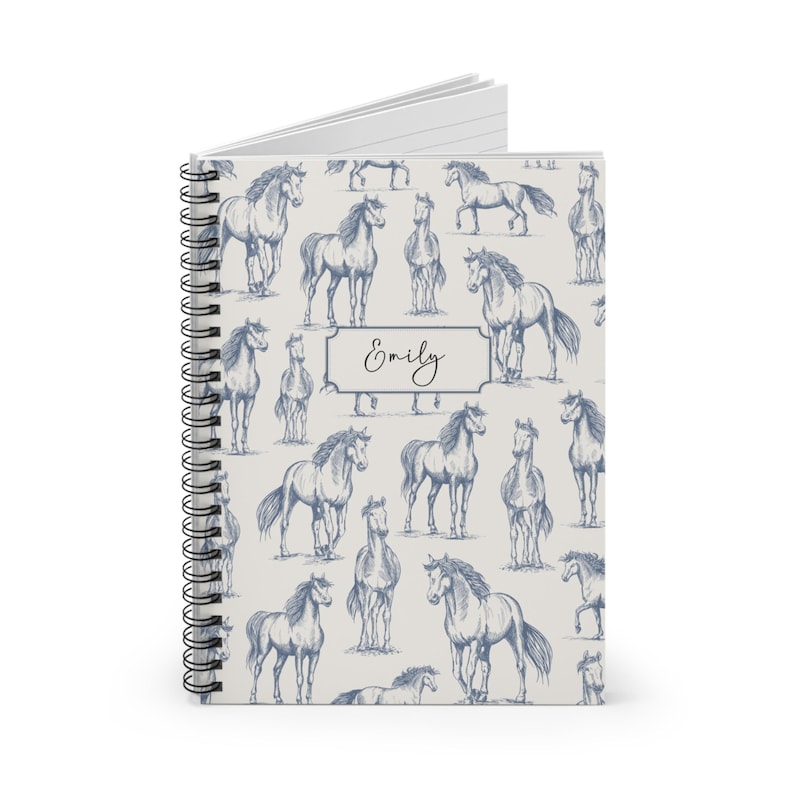 May include: A white spiral notebook with a blue and white horse pattern and the name "Emily" printed on the cover.