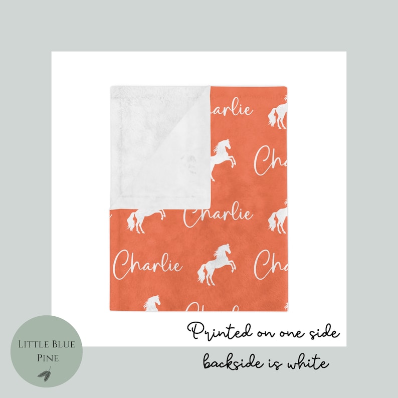 Pu&ograve; includere: Una coperta arancione con un motivo di cavalli bianchi e il nome "Charlie" in corsivo. Il lato inferiore della coperta &egrave; bianco e soffice. &Egrave; visibile anche il testo "Printed on one side, backside is white".