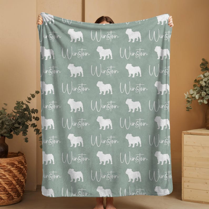 Person holding up a large custom English Bulldog blanket showing the repeating pattern of english bulldog silhouettes and the custom name in white on an aqua green background.