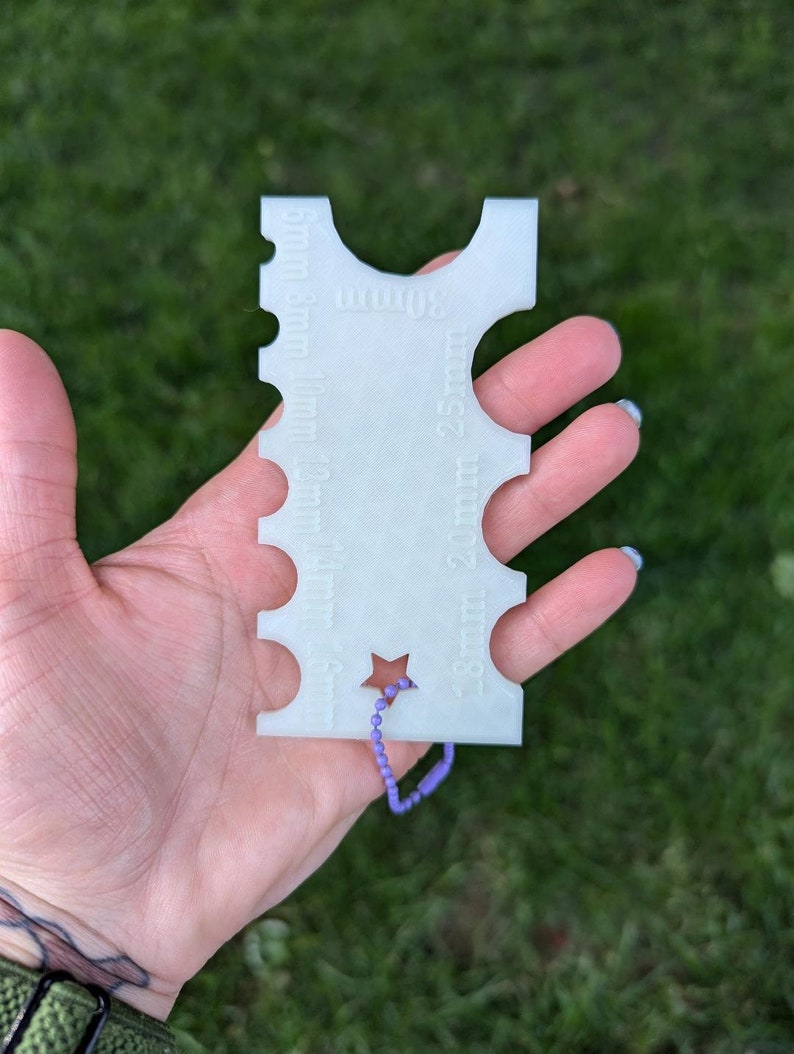 Peut inclure: Jauge en plastique blanc avec une d&eacute;coupe en forme d'&eacute;toile et une cha&icirc;ne violette attach&eacute;e. La jauge est gradu&eacute;e en 5 mm, 8 mm, 10 mm, 12 mm, 15 mm, 20 mm et 25 mm.