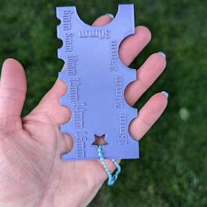 Peut inclure: Un porte-cl&eacute;s en plastique violet avec une &eacute;toile et une s&eacute;rie de trous de diff&eacute;rentes tailles. Le porte-cl&eacute;s est &eacute;tiquet&eacute; avec des mesures en millim&egrave;tres&nbsp;: 18&nbsp;mm, 20&nbsp;mm, 25&nbsp;mm, 30&nbsp;mm, 5&nbsp;mm, 8&nbsp;mm, 10&nbsp;mm, 12&nbsp;mm, 14&nbsp;mm, 16&nbsp;mm.