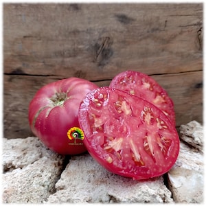 Puede incluir: Primer plano de un tomate rojo maduro, con uno cortado por la mitad para revelar el interior jugoso. El tomate descansa sobre una superficie de piedra, con un fondo de madera. El tomate tiene una pegatina que dice "MIRRAJOE".