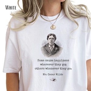 May include: A white t-shirt featuring a black and white portrait of Oscar Wilde. Below the portrait, the text reads: Some cause happiness wherever they go; others whenever they go. Mr. Oscar Wilde. A small black clover illustration is at the bottom.