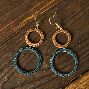Könnte beinhalten: Ein Paar handgefertigte Ohrringe mit zweistufigem Design. Die oberen Reifen sind warmbraun, während die unteren Reifen tief türkis sind. Die Ohrringe hängen an goldfarbenen Ohrhaken und zeigen einen Bohemian-Stil.