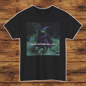 May include: Black t-shirt featuring a graphic of a frog dressed as a wizard riding a horse, with the text "3 MANA POTIONS NO LUNCH". The frog is wearing a pointed hat and cape, holding a sword.