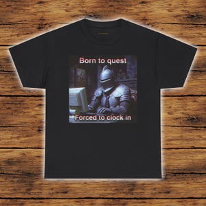 May include: Black t-shirt featuring a knight in armour at a computer, with the text "Born to quest" and "Forced to clock in". The image is a humorous take on modern work life, contrasting medieval imagery with office culture.