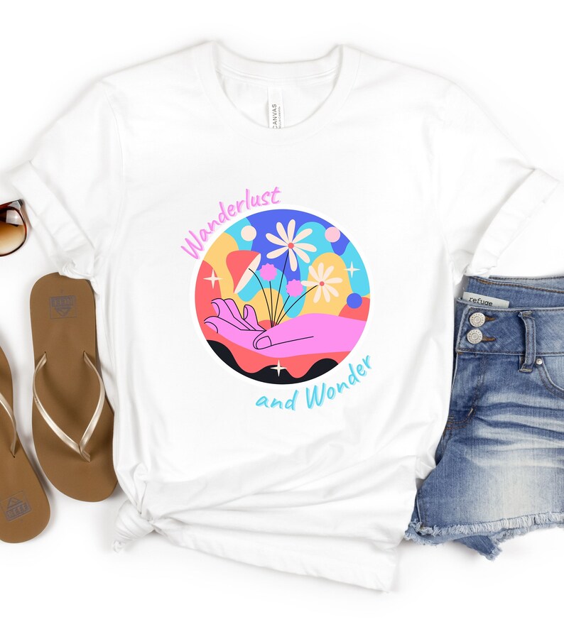 May include: White t-shirt with a colorful graphic design of a hand holding flowers. The graphic is surrounded by a circle with the text "Wanderlust and Wonder".