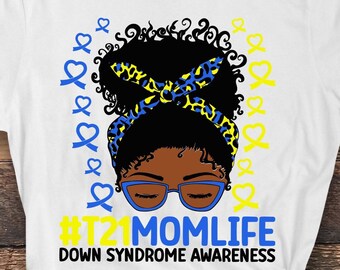 Puede incluir: Camiseta blanca con un gráfico negro y amarillo de una mujer con una diadema de cinta azul y amarilla. El texto '#T21MOMLIFE DOWN SYNDROME AWARENESS' está impreso en la camiseta.