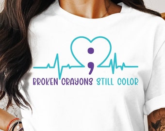 May include: White t-shirt with a teal blue heartbeat graphic and a purple heart with a teal blue semicolon inside. The text "BROKEN CRAYONS STILL COLOR" is printed below the graphic.