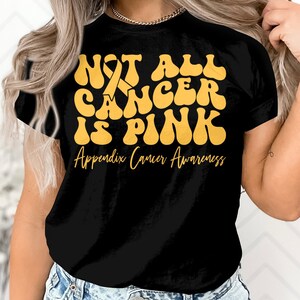 Puede incluir: Camiseta negra con el texto "NOT ALL CANCER IS PINK" en amarillo, con un lazo amarillo. Debajo, el texto "Appendix Cancer Awareness" en letra más pequeña. La camiseta es de cuello redondo.