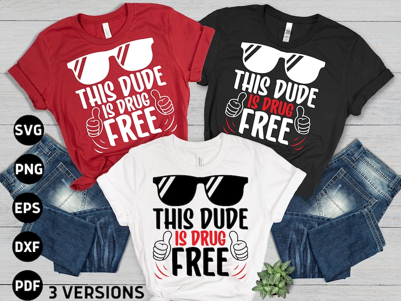 May include: Three t-shirts in red, black, and white, each with the text "THIS DUDE IS DRUG FREE" in a bold, playful font. The design includes sunglasses and a thumbs-up gesture. The shirts are displayed with blue jeans.