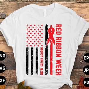 Peut inclure: T-shirt blanc avec un motif de drapeau américain vieilli, avec des étoiles rouges et des rayures noires. Il comprend un ruban rouge et le texte "RED RIBBON WEEK" et "NOBODY FIGHTS ALONE".