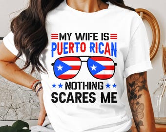 May include: White t-shirt with the text "MY WIFE IS PUERTO RICAN NOTHING SCARES ME." The design includes sunglasses with the Puerto Rican flag and blue stars.