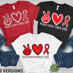 May include: Three t-shirts in red, black, and white, each featuring a peace sign, a heart, and a ribbon, with the text "PEACE LOVE DRUG FREE". The image also includes file format icons: SVG, PNG, EPS, DXF, and PDF, with the text "3 VERSIONS".