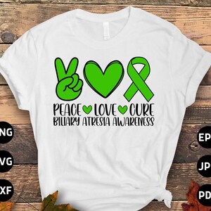 Op de afbeelding: Wit T-shirt met een groen vredesteken, hart en lint. De tekst "Peace Love Cure Biliary Atresia Awareness" staat op het T-shirt gedrukt.