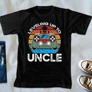 Könnte beinhalten: Schwarzes T-Shirt mit einer Retro-Grafik eines Videospiel-Controllers und dem Text "Leveling Up To Uncle".