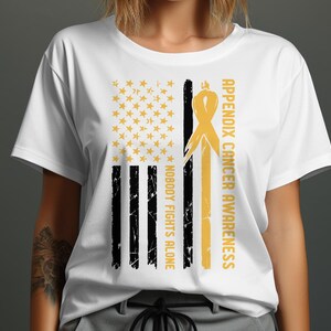 Puede incluir: Camiseta blanca con un diseño de bandera estadounidense desgastada. La bandera es amarilla y negra con una cinta dorada y el texto "Appendix Cancer Awareness Nobody Fights Alone".