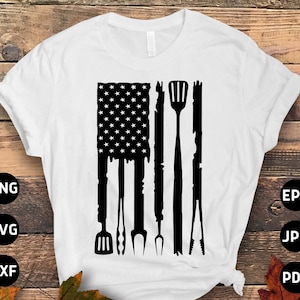 May include: A white t-shirt with a black silhouette of an American flag. The flag is made up of grilling tools, such as a spatula, tongs, and a fork.