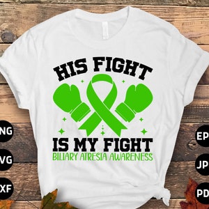 Op de afbeelding: Wit T-shirt met de tekst "HIS FIGHT IS MY FIGHT" in zwart, met groene bokshandschoenen en een groen lint. De woorden "BILIARY ATRESIA AWARENESS" zijn groen. Het shirt staat op een houten achtergrond.