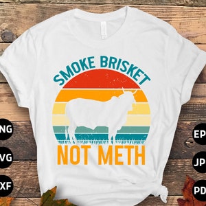 Op de afbeelding: Wit T-shirt met een retro-stijl grafische afbeelding van een koe en de tekst "Smoke Brisket Not Meth".