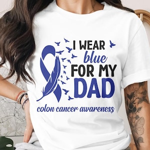 Puede incluir: Camiseta blanca con una cinta azul y el texto "Uso azul por mi papá conciencia del cáncer de colon".