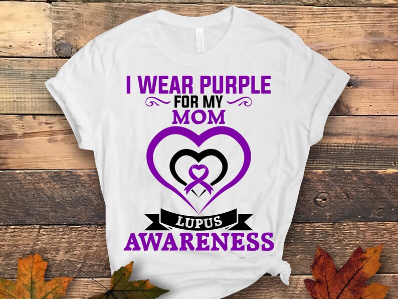 May include: White t-shirt with a purple ribbon in a heart shape and the text "I wear purple for my mom Lupus Awareness".