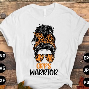 May include: White t-shirt with a graphic of a messy bun hairstyle, sunglasses, and a leopard print headband. The text "CRPS WARRIOR" is below the graphic in black. The shirt is displayed on a wooden background.