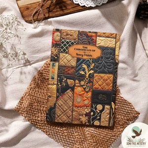 May include: A book titled "The Chronicles of" by Nancy Pebbles. The cover features a patchwork design with various shades of brown, gold, and black. The design includes intricate floral patterns and quilted squares.