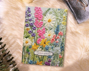 May include: A light blue journal with a floral embroidery design. The flowers are pink, yellow, blue, purple, and white. The journal has the text "My Garden of Gratitude" on the front.