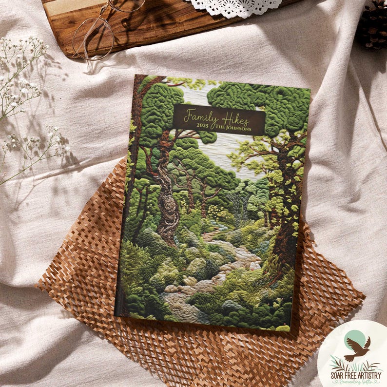 My newest whimsical woodland forest aesthetic journal called, Woodland Wanderer. It is displayed on a cream outdoor picnic blanket. This dark green journal has a rustic aesthetic. A perfect forest gift for family hiking and PNW trail notes.
