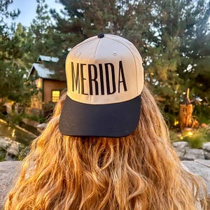 Könnte beinhalten: Eine weiße Keramik-Tasse mit schwarzem Henkel und dem Text "But First, Coffee" in schwarzer, handschriftlicher Schrift. Die Tasse steht auf einer weißen Oberfläche.